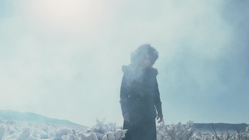 A man in heavy clothing and a fur hat stands in the snow on a cold sunny day