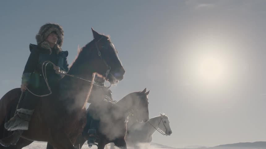 Three people ride horses across an icy landscape