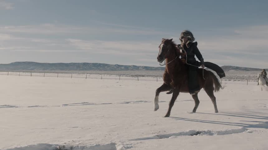 A man in a fur hat rides a horse through the snow