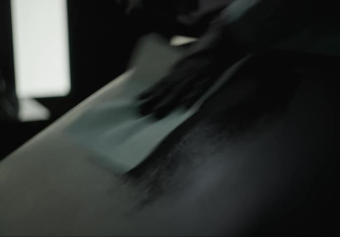 A gloved hand spraying and cleaning a surface with a paper towel