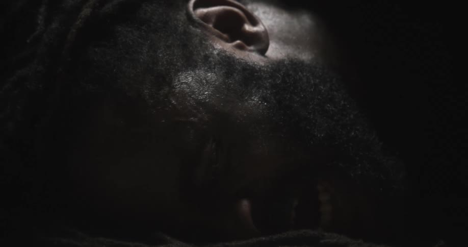 A man is lying with his face against the ground crying and moaning in the darkness