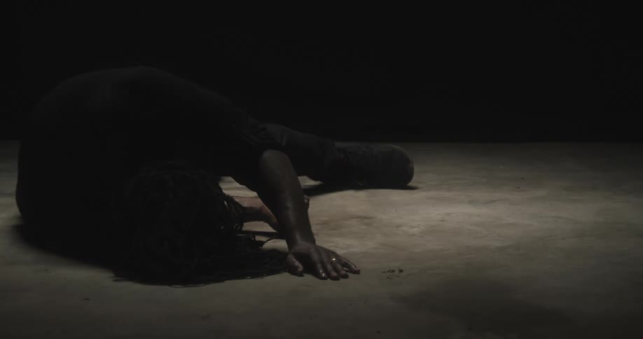 Person lies on their side on the ground in dimly lit area