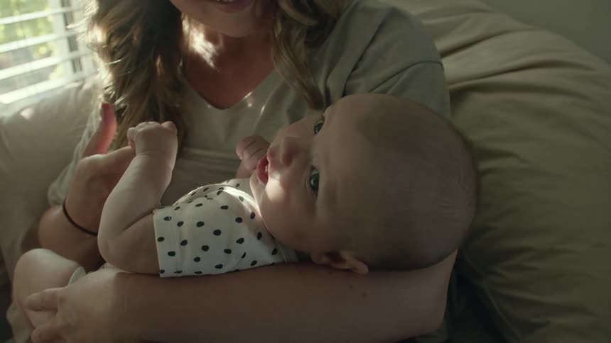 A smiling mother holding her infant on a sofa