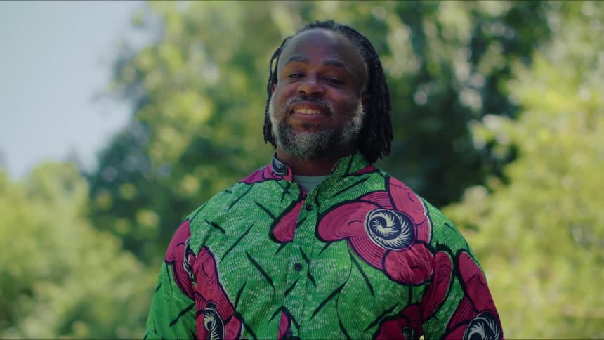 A man is standing amongst the trees and smiling