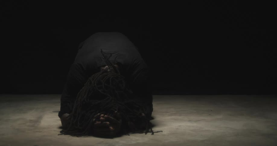 Person kneeling in dim area places their head on theirhand and on the floor