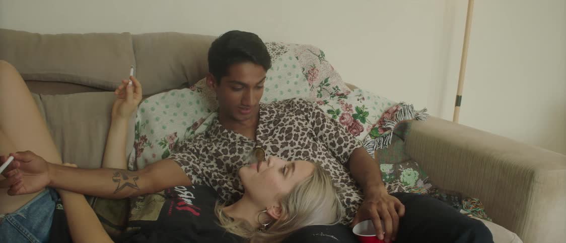 A woman is laying on a mans lap on a couch as they smoke cigarettes