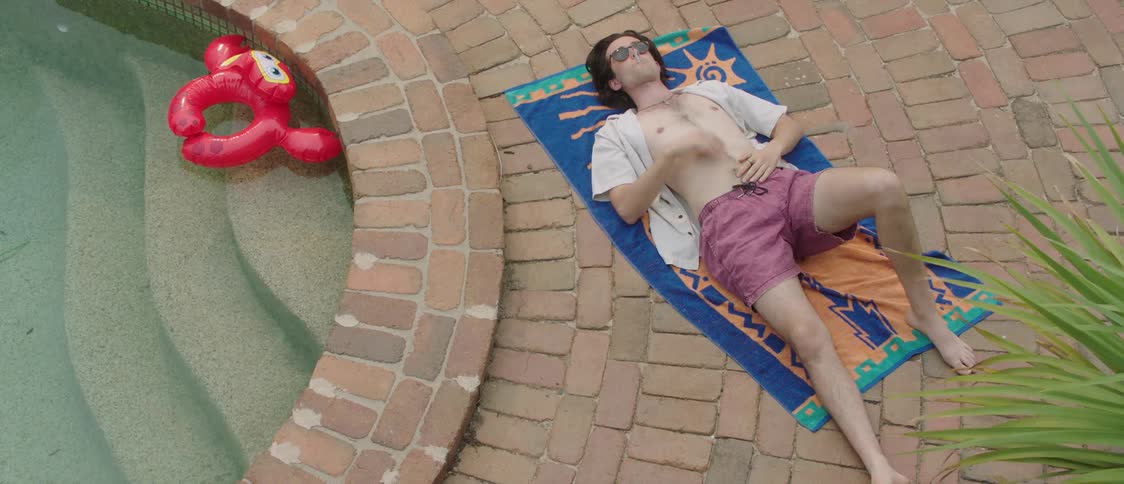 A man smokes as he lays on a beach towel next to a pool