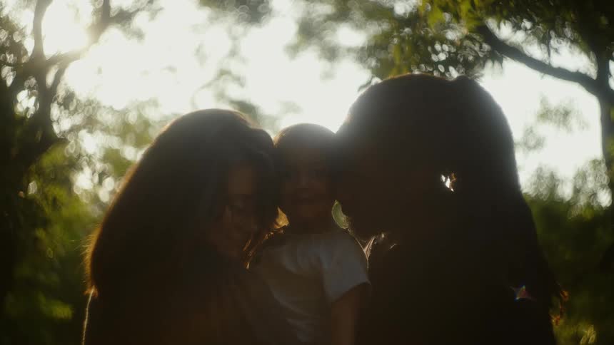 Two women are holding a baby under some trees
