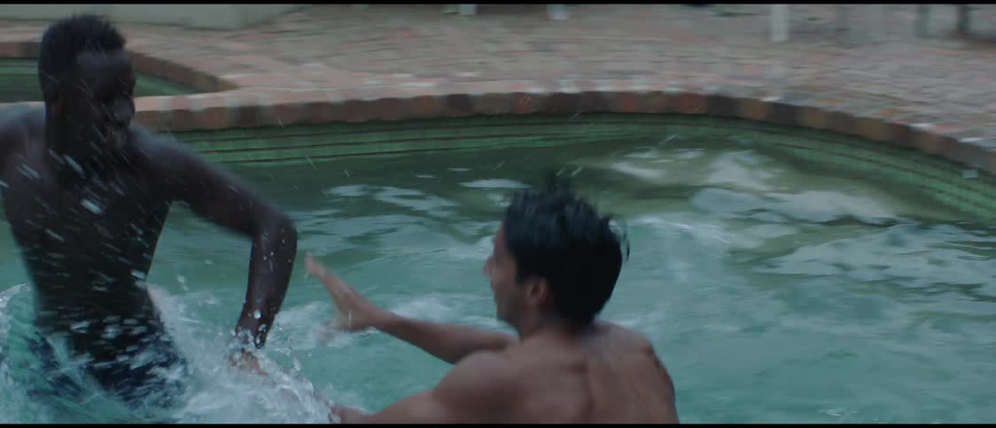 A man is in a swimming pool drinking a bottle of wine and he swims away from another man who takes the bottle and they are playing to get the bottle