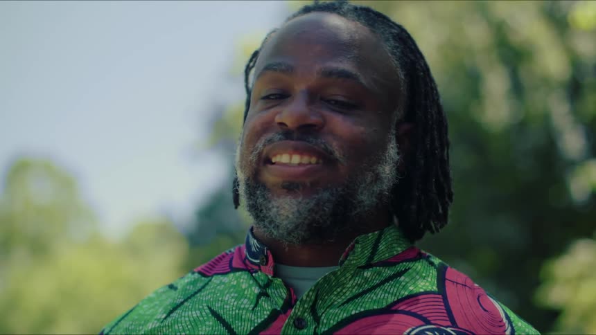 A man wearing a brightly colored top turns his head smiling and full of joy