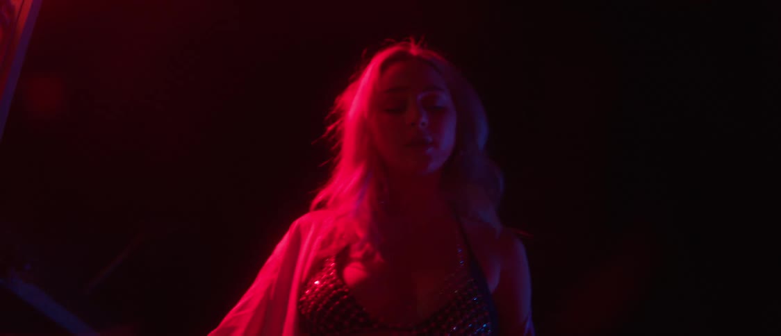Woman carrying bottle of alcohol walks under bright pink colored lighting at night