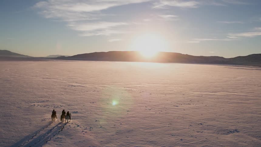Three people horseback ride at dawn