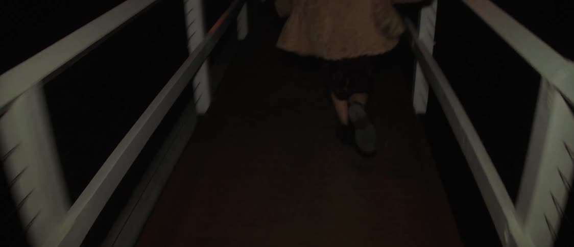 Blonde woman with brown coat runs along timber bridge at night