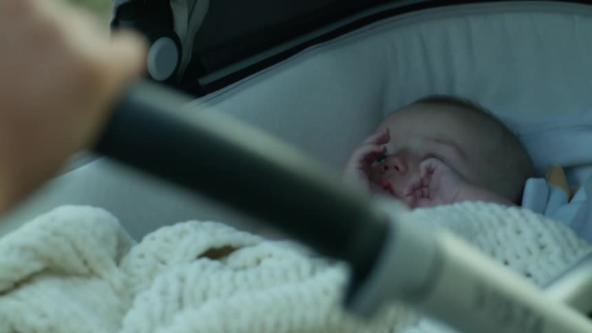 Baby lying in baby stroller sucks thumb while being pushed along track near grass
