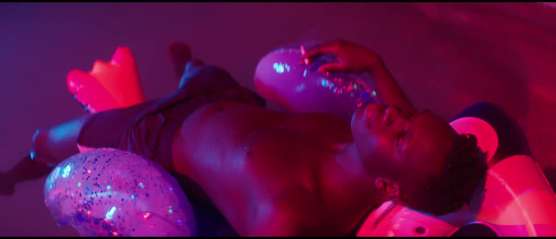 Shirtless black man lying on the float in a small pool smoking a cigarette