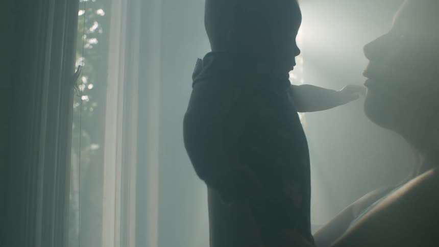 Mother holding baby up is silhouetted against the sunlight streaming through windows