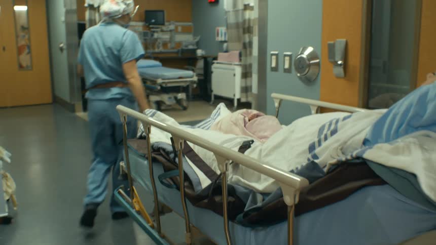 Mother and swaddled baby are moved together on hospital bed by hospital personnel