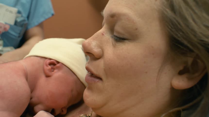 A woman has just had a baby and is holding himher in her arms while a nurse turns the babys head so it is more facing the mother