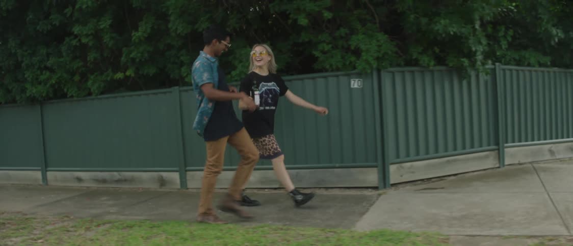 A man and woman drinking wine from a bottle while taking a walk in a neighborhood