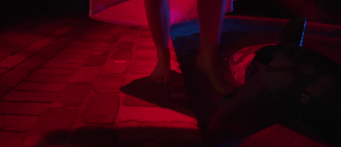 At night woman wearing pink walks along edge of pool nudging nearby pool float