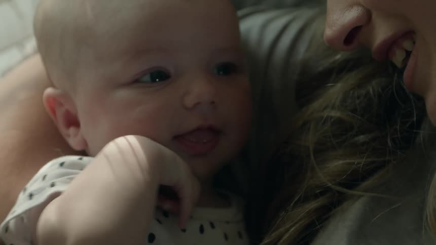 Mother resting at home near a window talks to her happy smiling newborn baby