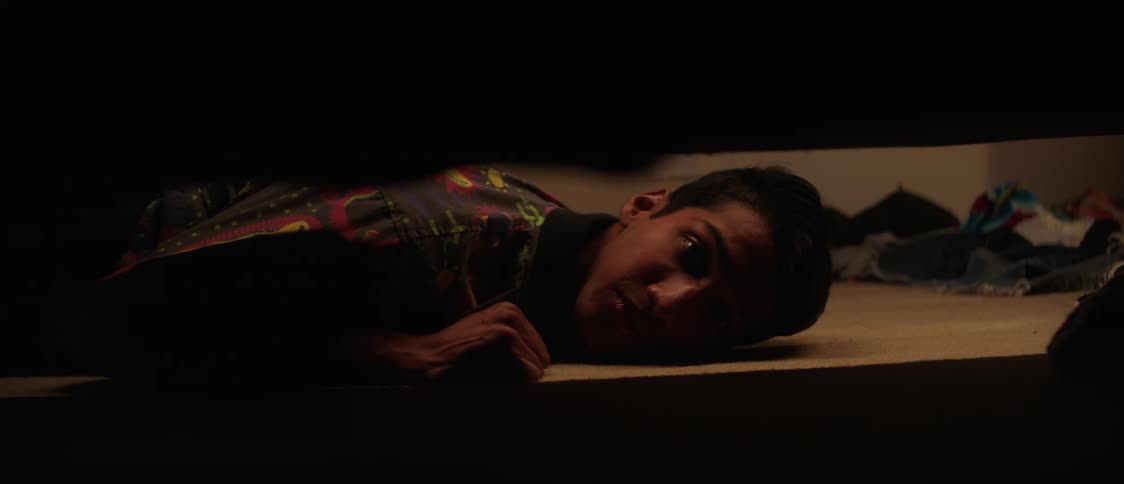 A young man lying on the floor looking under the bed