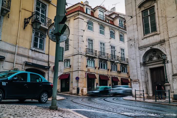 People walk on the pavements and vehicles drive down the street next to apartment buildings in the city
