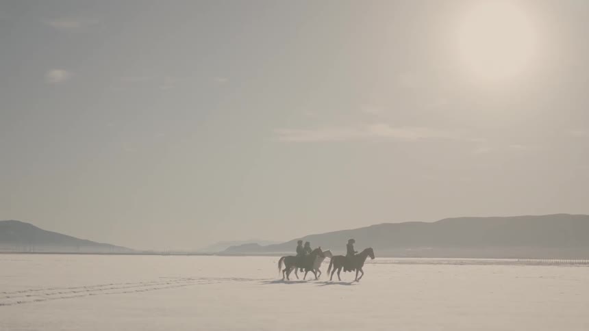 Three men riding horses across a snow-covered landscape near a mountain range