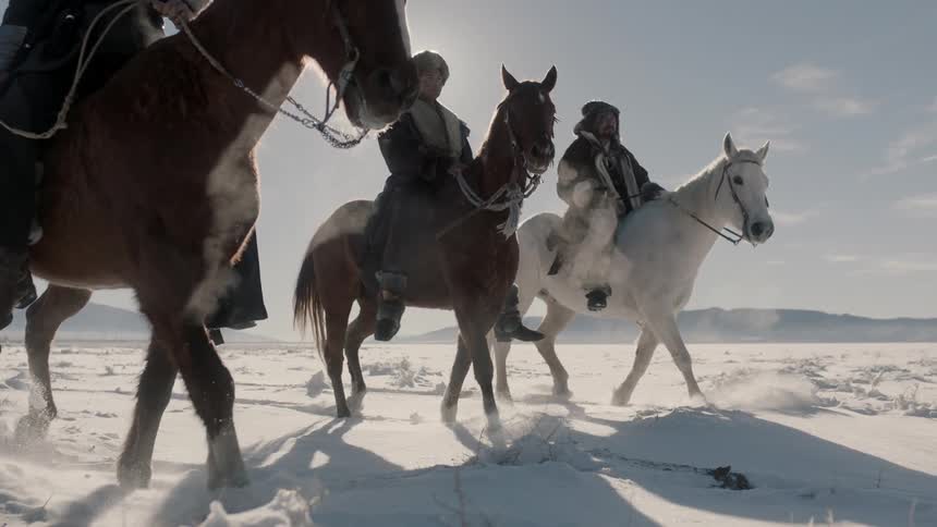 People ride their horses on a snow covered field
