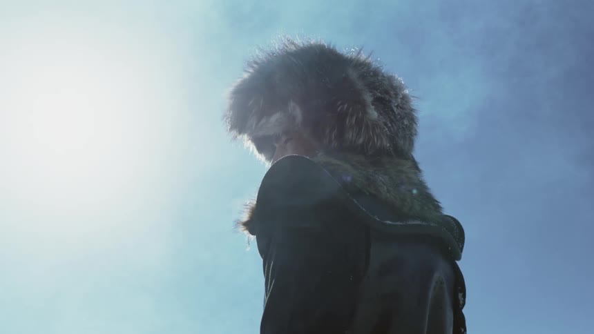 A person in a fur hat stands in the sunlight