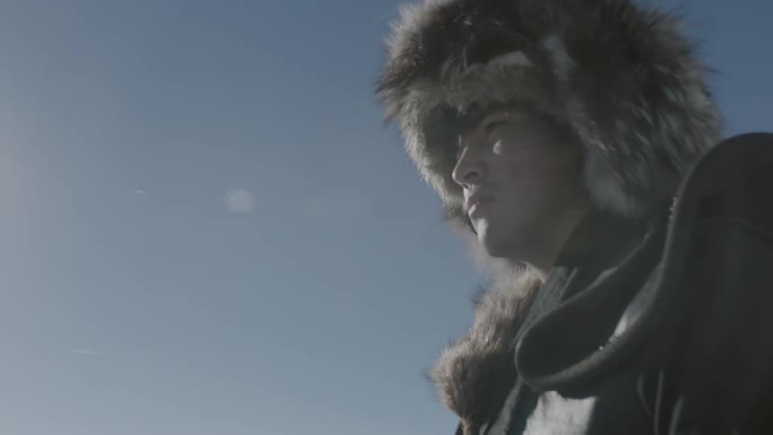 A man in a fur hat walks beneath a bright blue sky