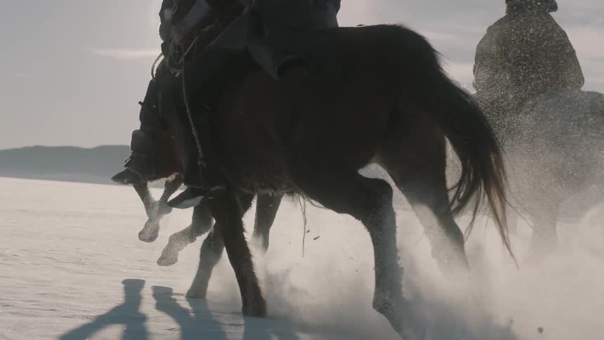 Horses with riders running across a snowy plain