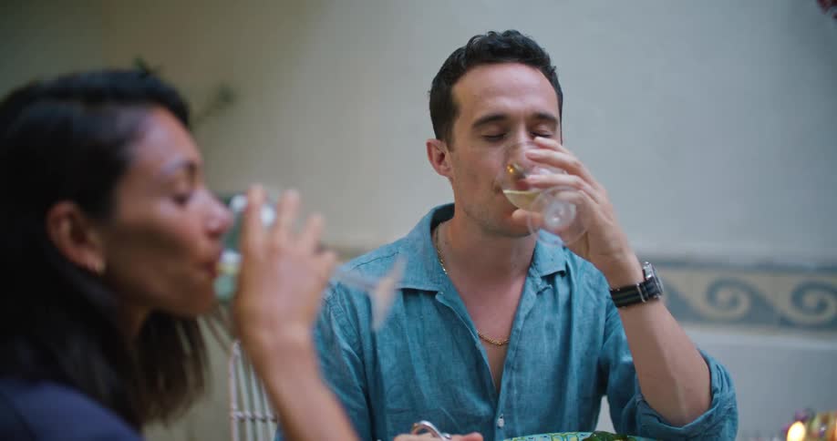 A man and woman raising wine glasses and drinking during dinner