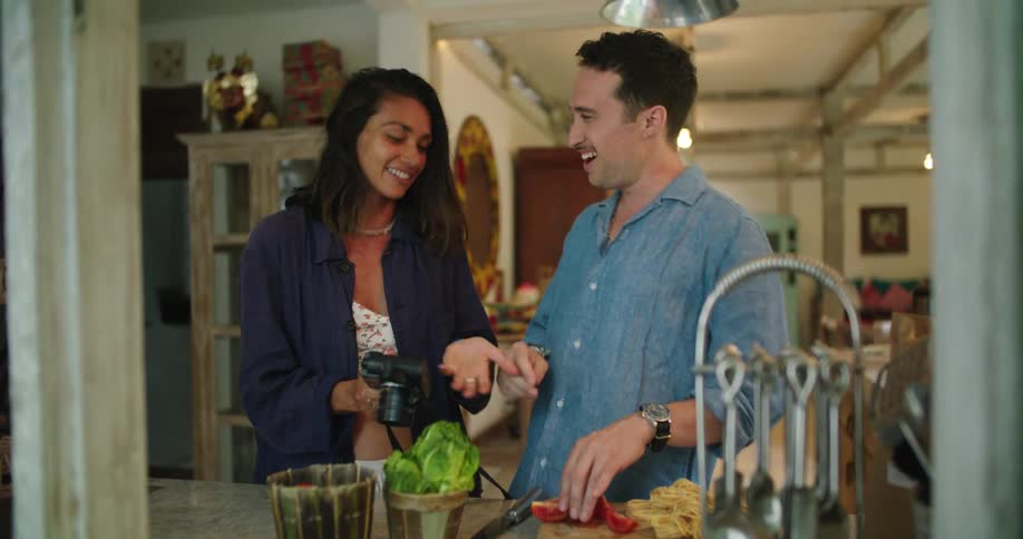 Young couple cooking in the kitchen at home laugh while looking at pictures on a camera