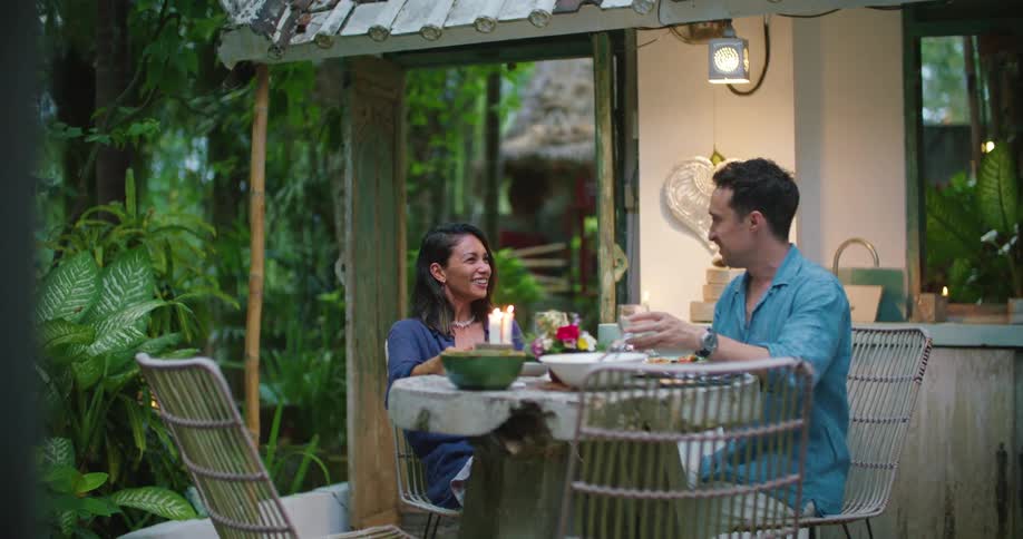 A couple sitting at an outdoor table for a candlelight meal laughing and teasing each other
