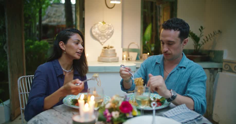 Man and woman talk while eating pasta at an outdoor table