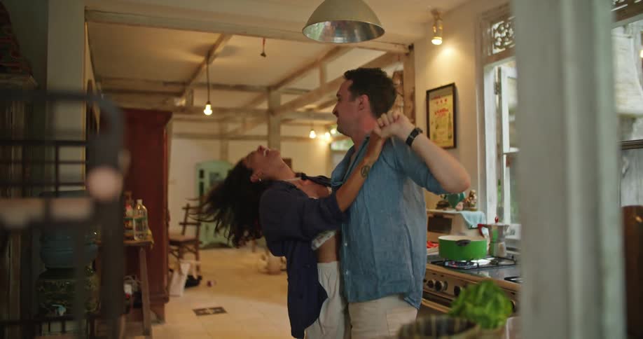 Man and woman dance in kitchen as pot sits on lit gas stove