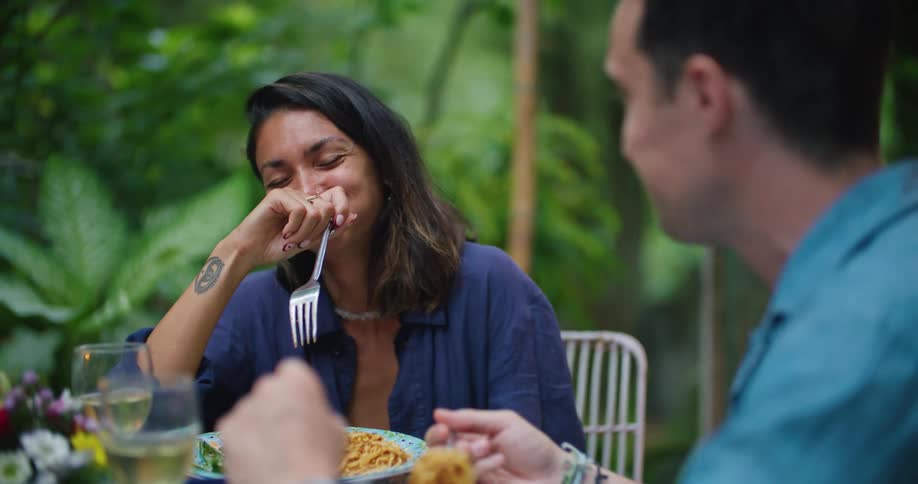 Woman eating at outdoor table with man covers her mouth as she laughs