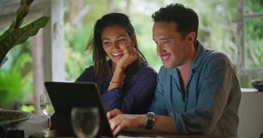 A man and woman sitting side by side looking at a laptop smiling and talking