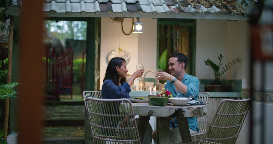 A man and woman clink wine glasses in a toast while dining on their deck