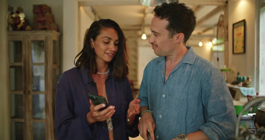 Young couple cooking in the kitchen at home talk while looking at pictures in the phone