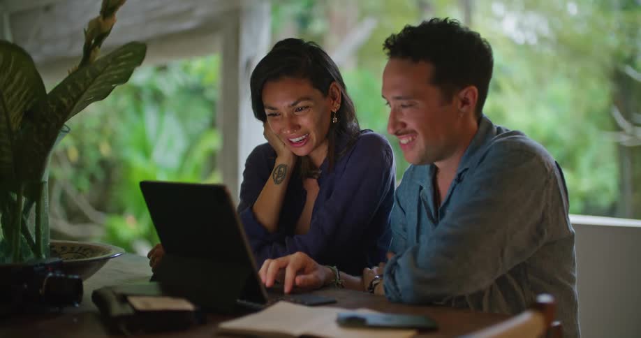 A man and a woman are sitting together at a table with a laptop computer talking and looking at the screen
