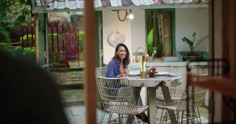 Young happy woman sitting at a table in the backyard waiting for her husband