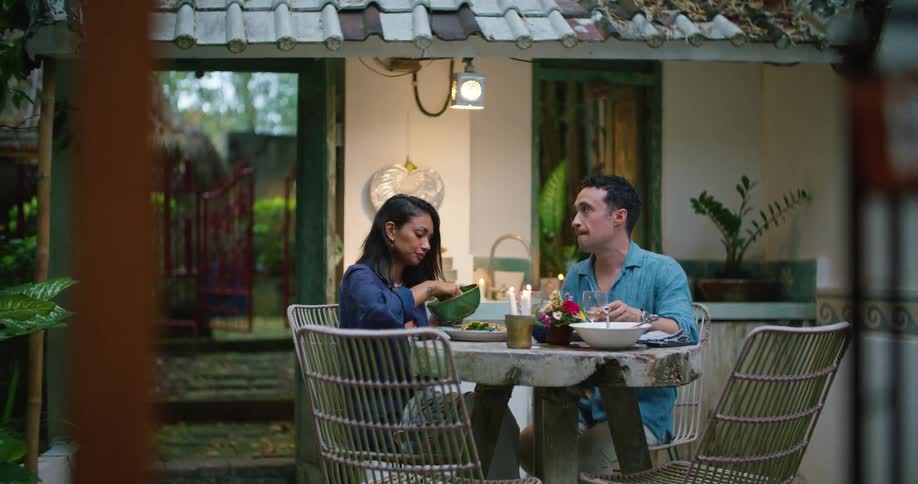 A man and woman dining outside on the patio talking and sipping wine