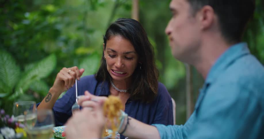 Young happy couple laugh and talk while eating a hearty meal in the backyard