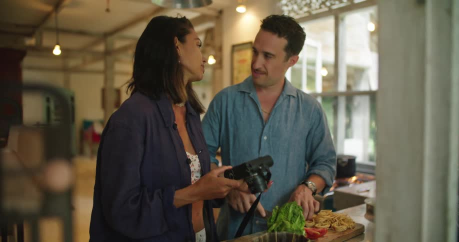 Happy young couple cooking at home talk and laugh looking at pictures in a camera