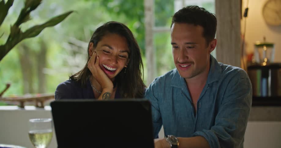 Young happy couple talking and smiling while browsing a laptop on the dining room at home