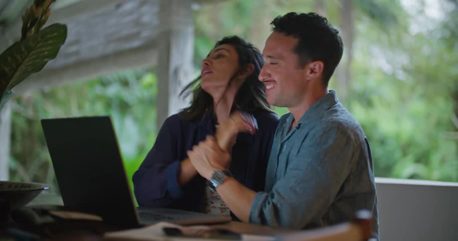 A man and a woman are sitting together at a table with a laptop computer talking and looking at the screen