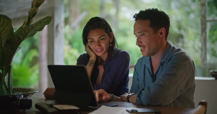 A man gestures with his hand as he talks with a woman sitting beside him and describes what is on the laptop