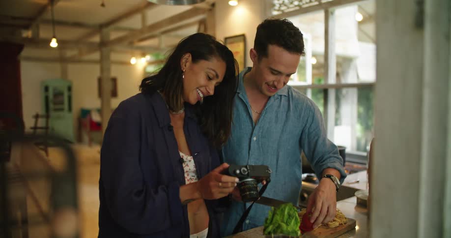 A man and a woman are standing together talking as she shows him her camera